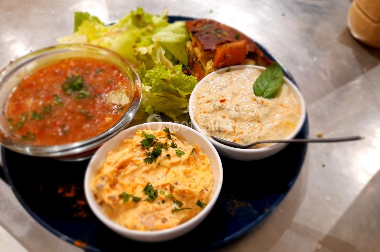 Assiette contenant trois bols de sauces variées, accompagnée de salade verte et d'une part de pain ou gâteau salé.