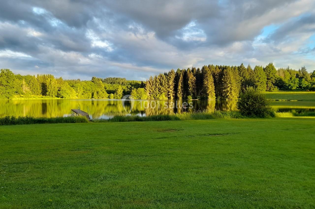 Paysage avec un lac entouré de pelouses verdoyantes et de forêts sous un ciel partiellement nuageux.