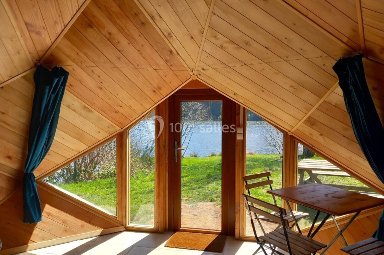 Vue intérieure d'une cabane en bois avec une porte vitrée donnant sur un lac et un espace extérieur verdoyant.