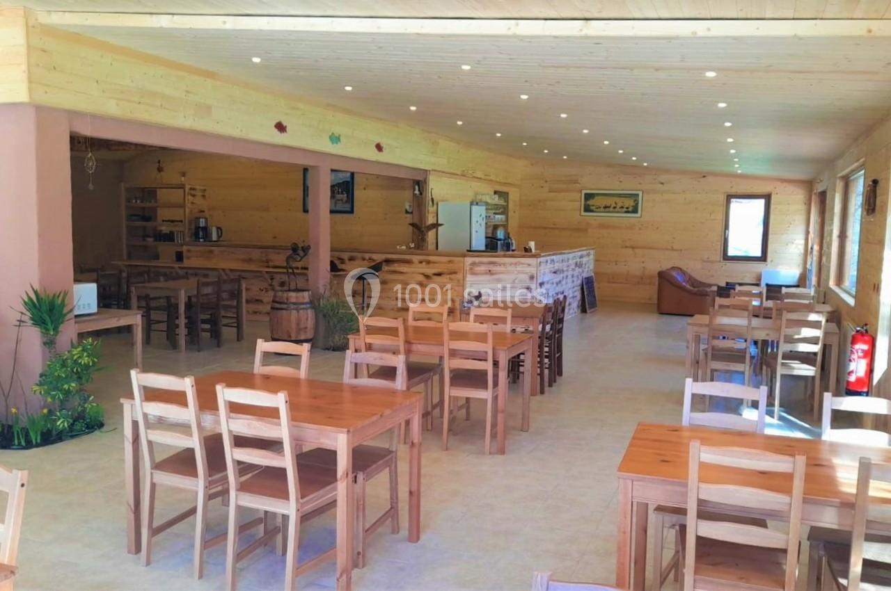 Salle lumineuse avec des tables et chaises en bois, décorée de plantes et éclairée par des spots au plafond.