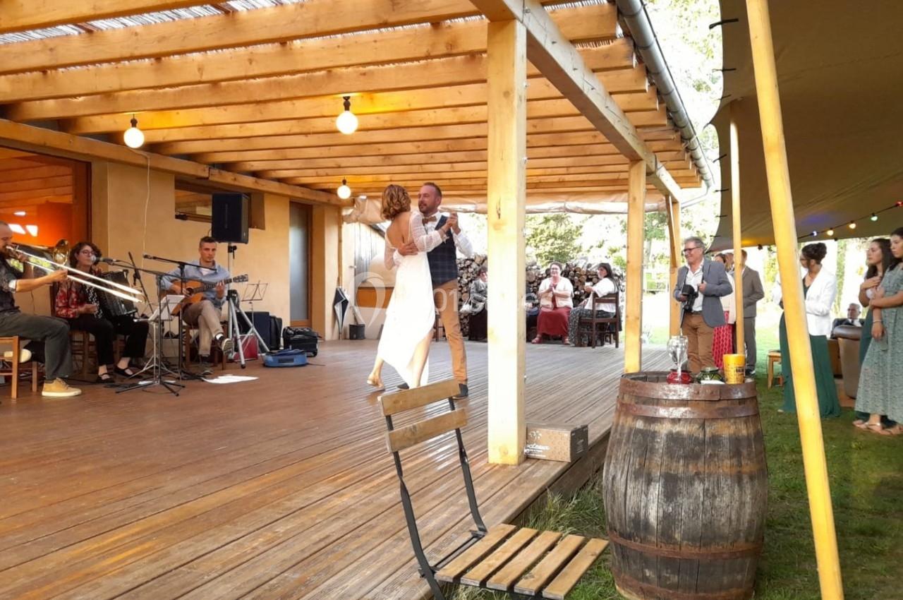Un couple danse sur une terrasse en bois, accompagné d'un groupe de musiciens, lors d'une fête en plein air.
