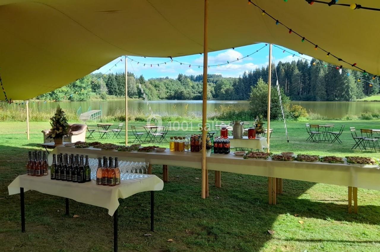 Buffet en plein air sous une tente avec vue sur un lac et des chaises disposées sur une pelouse verdoyante.