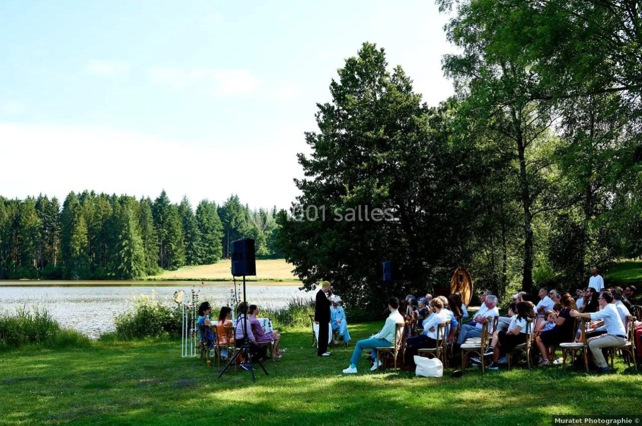 Un groupe de personnes assises en plein air près d'un lac, entouré d'arbres, lors d'un événement.