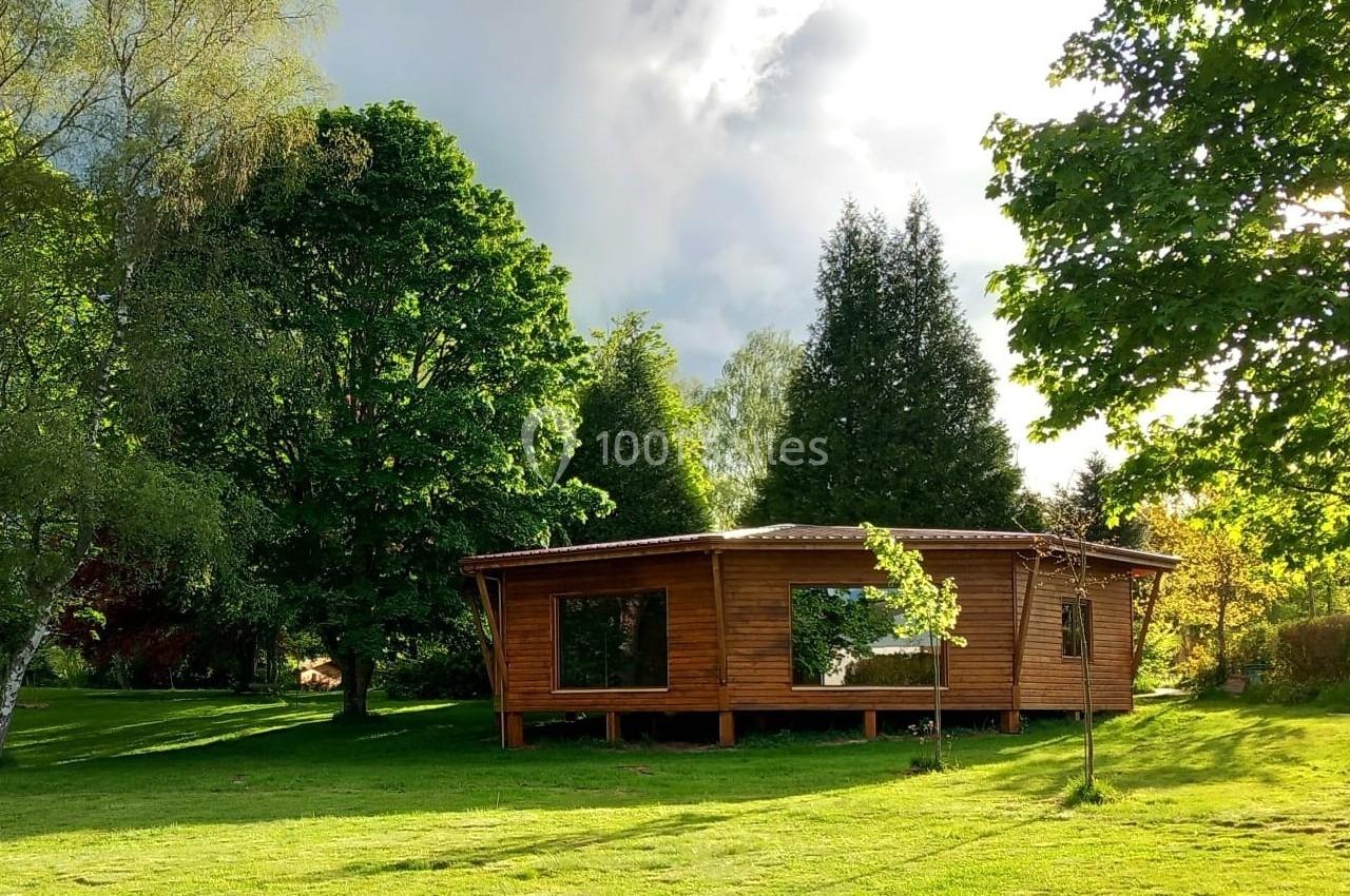 Cabane en bois entourée d'arbres et d'une pelouse verdoyante sous un ciel partiellement nuageux.