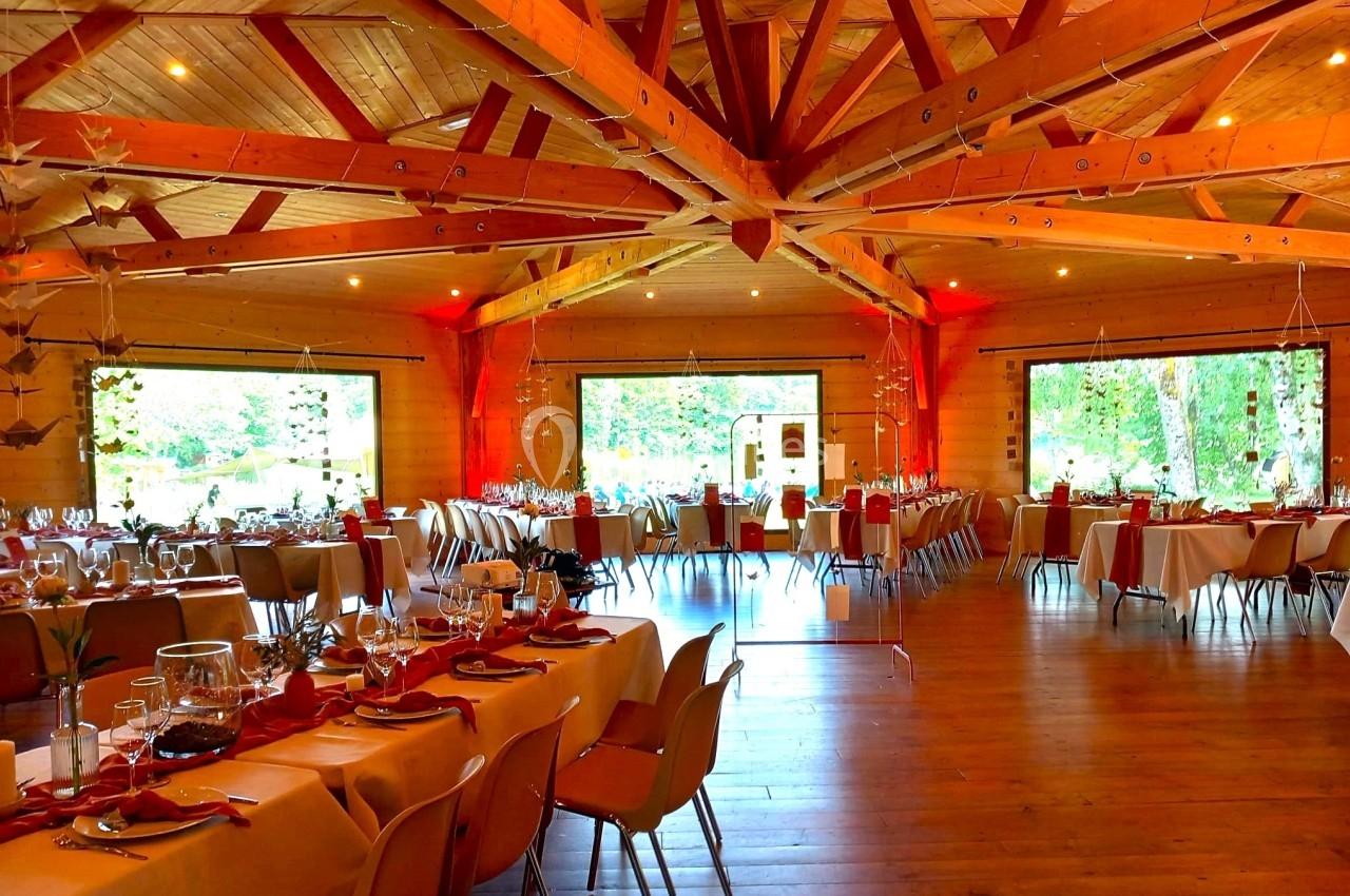 Salle en bois avec de grandes baies vitrées, tables dressées pour un repas, éclairage chaleureux et décorations suspendues.