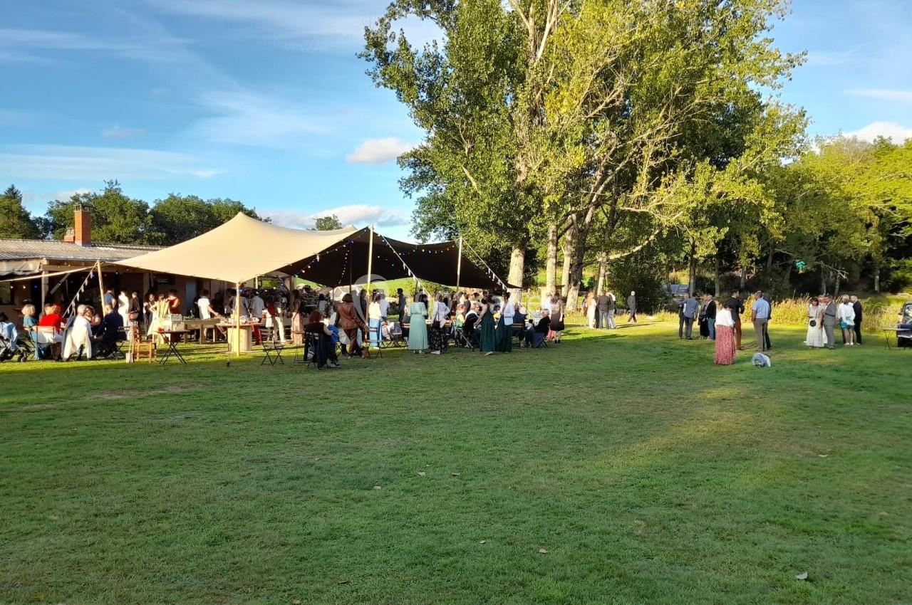 Groupe de personnes réunies sous une grande tente beige dans un espace extérieur verdoyant par temps ensoleillé.