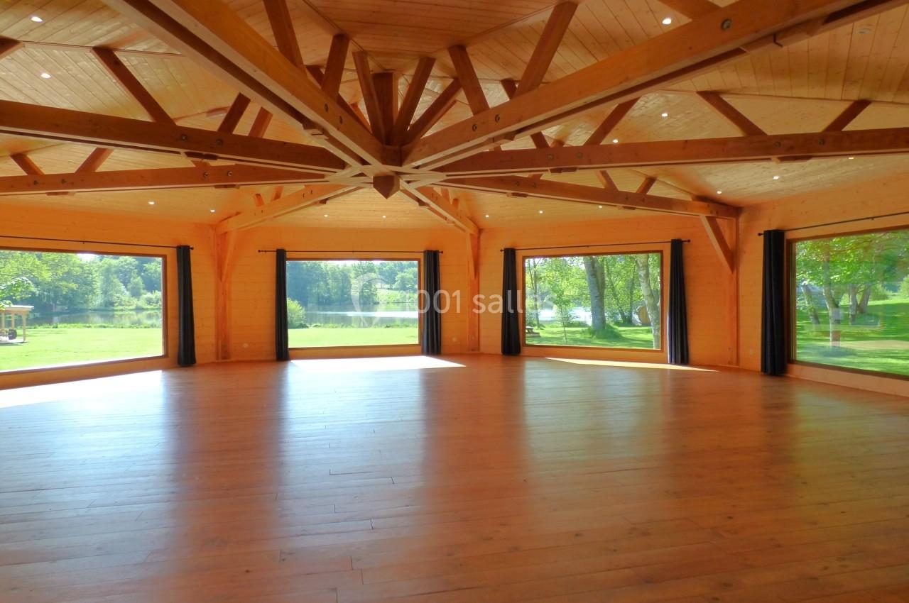 Salle spacieuse en bois avec de grandes baies vitrées donnant sur un paysage verdoyant et lumineux.