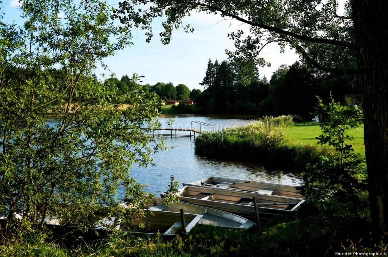 Barques amarrées au bord d'un lac entouré de verdure, avec un ponton en arrière-plan sous un ciel dégagé.
