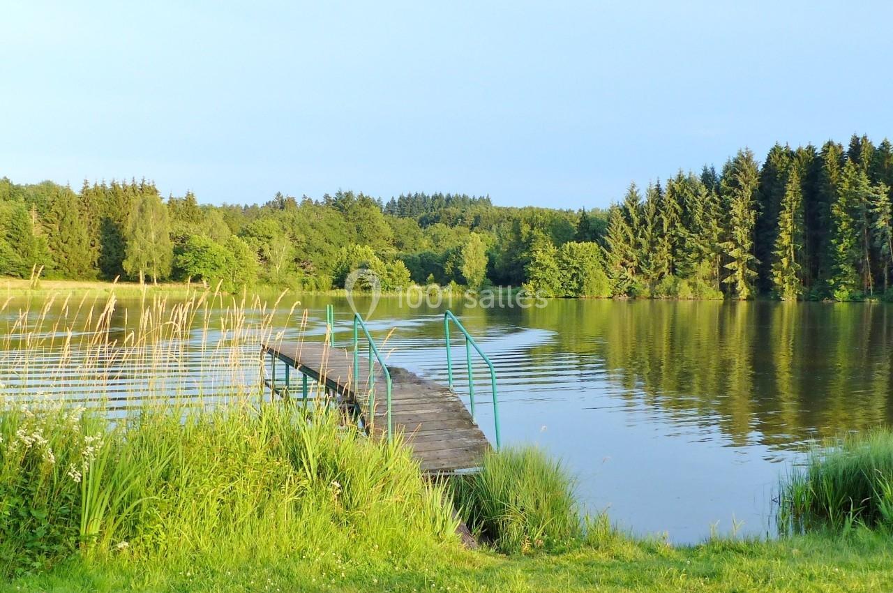 Ponton en bois s'avançant sur un lac entouré de végétation et de forêts sous un ciel dégagé.