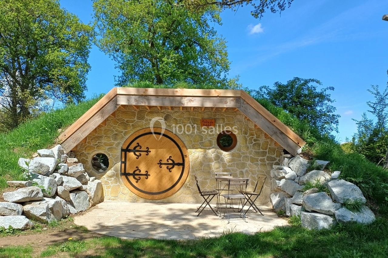 Entrée d'une maison semi-enterrée en pierre avec une porte ronde en bois, entourée de verdure et de rochers.