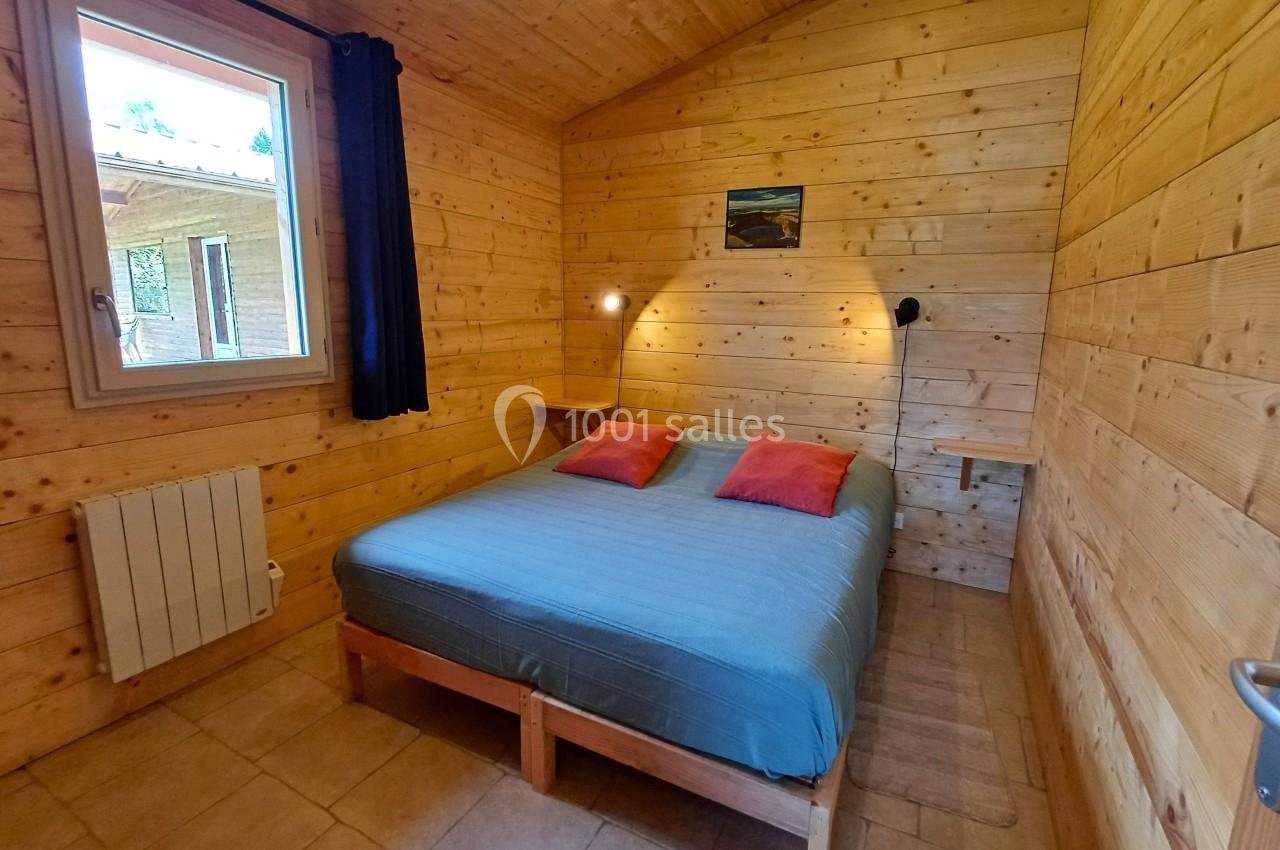 Chambre en bois avec un lit double, deux coussins rouges, une fenêtre et un éclairage mural.