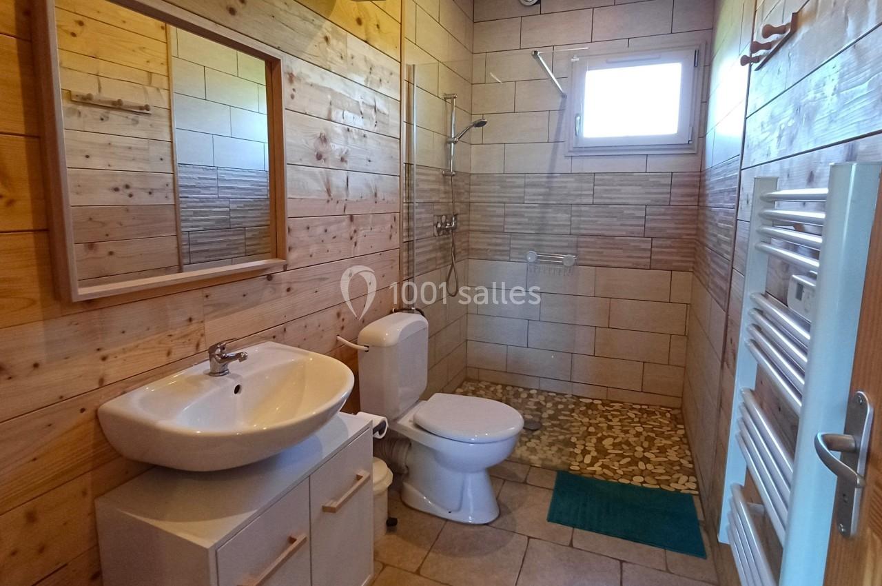 Salle de bain avec murs en bois, lavabo, toilettes, douche à l'italienne, radiateur et fenêtre apportant de la lumière…