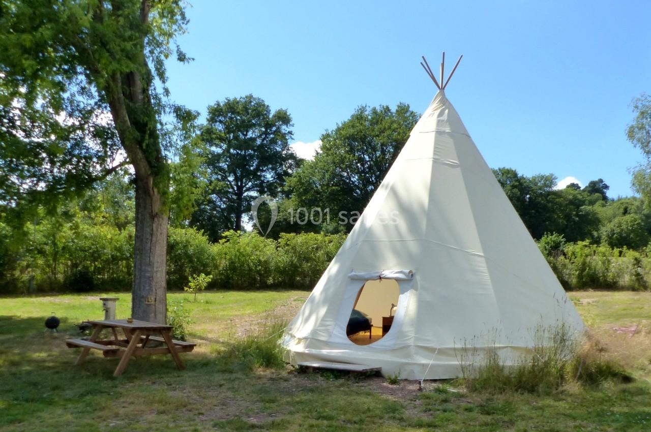 Tente tipi blanche installée sur une pelouse avec une table de pique-nique à proximité, entourée de verdure.