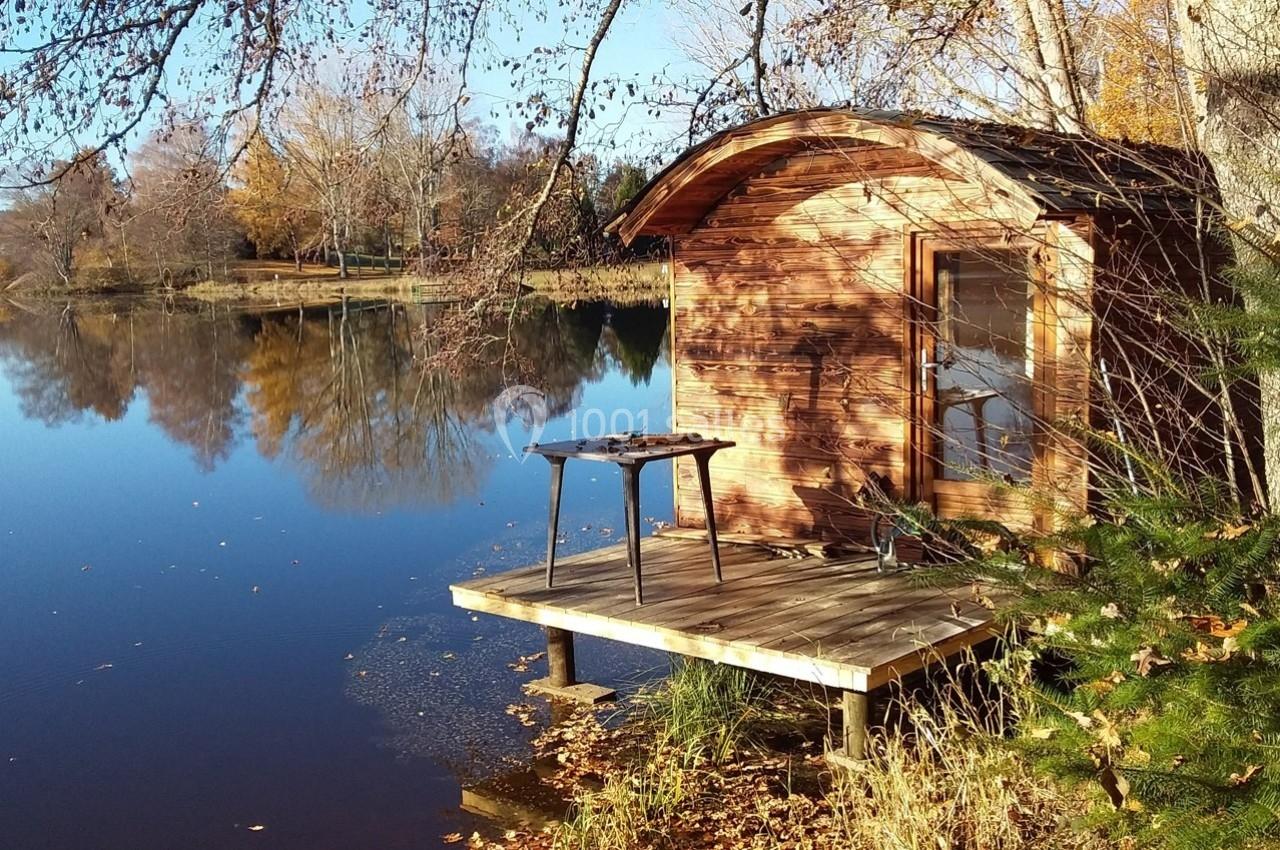 Cabane en bois au bord d'un lac calme entouré d'arbres aux couleurs automnales.