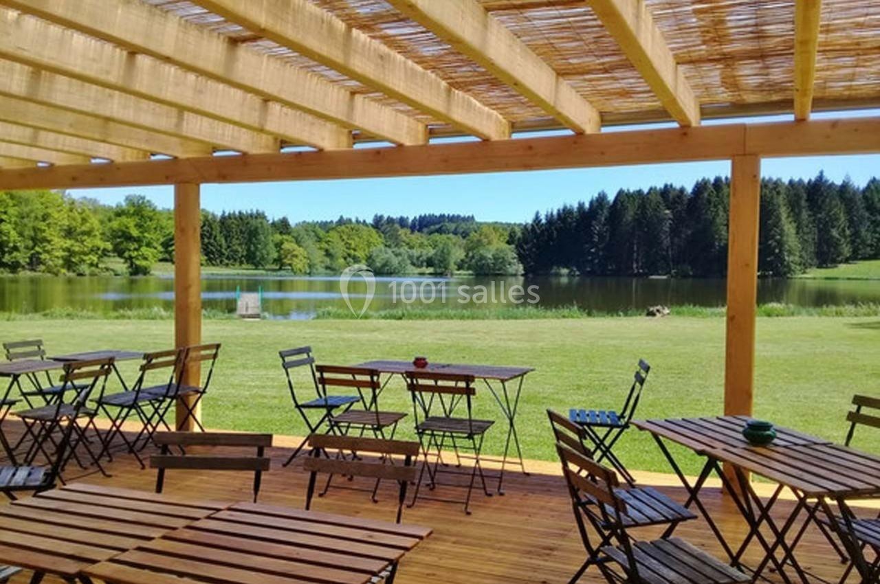 Terrasse en bois avec tables et chaises donnant sur un lac entouré de pelouses et de forêts.