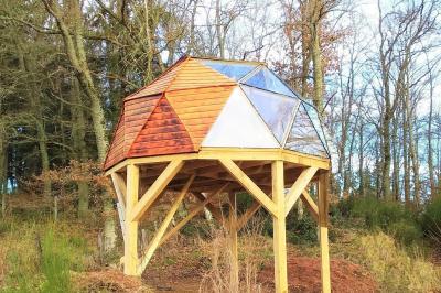 Cabane en bois avec toit en tuiles grises, grandes fenêtres et porte vitrée, située dans un espace arboré.