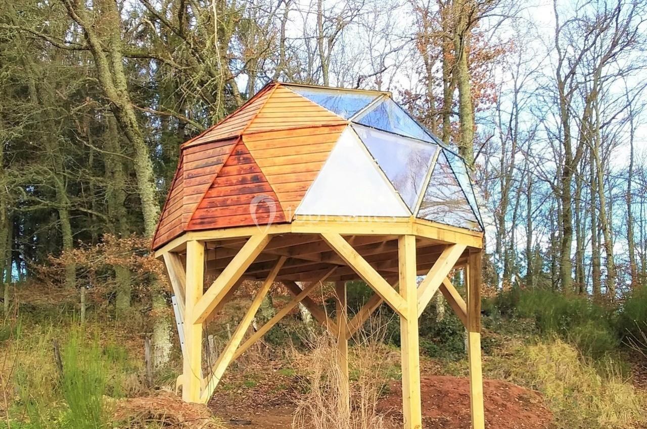 Structure géodésique en bois et verre surélevée sur pilotis, située dans une clairière boisée.