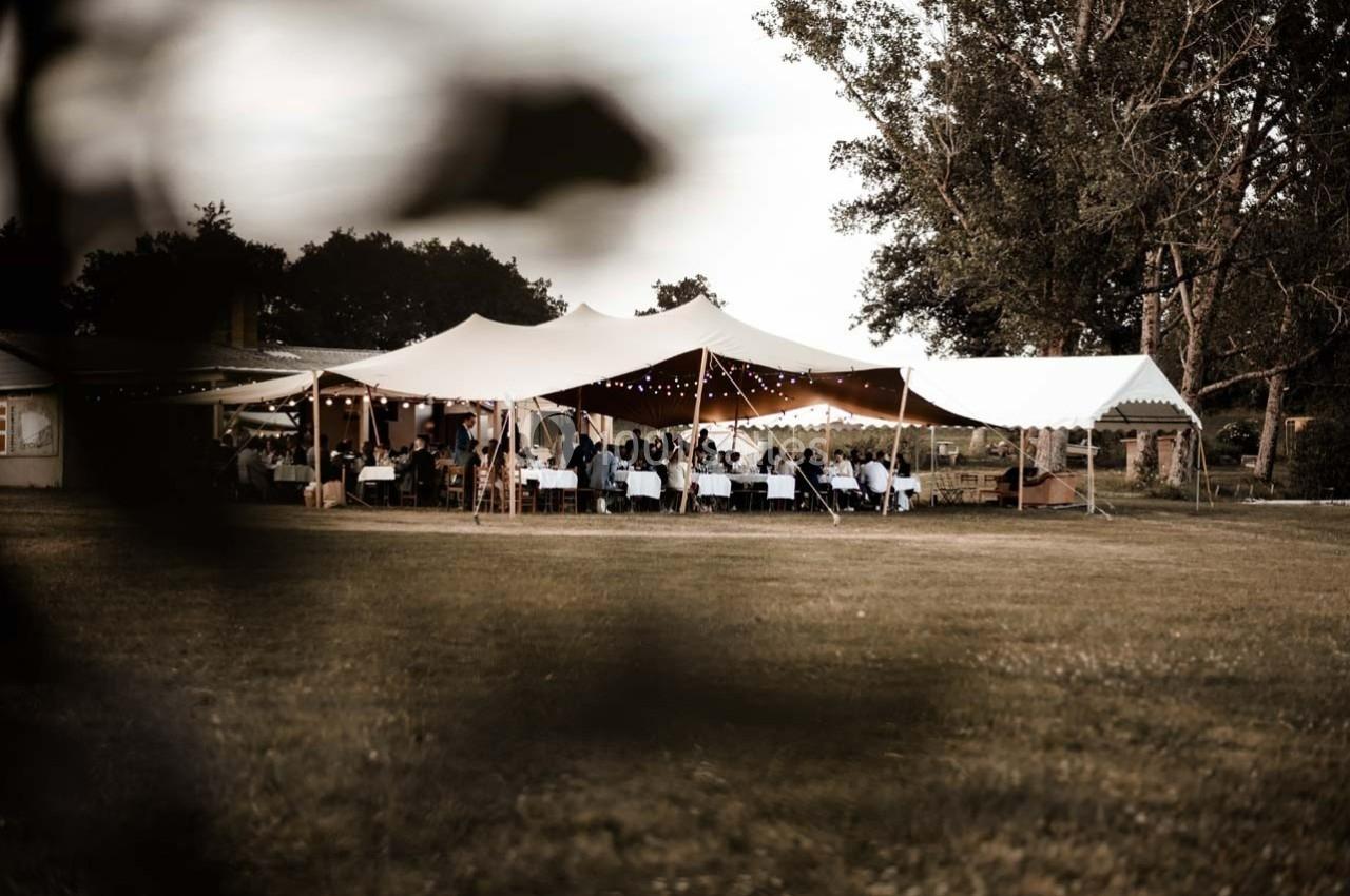 Tente blanche installée en extérieur avec des tables et des invités, entourée d'arbres et d'une pelouse.