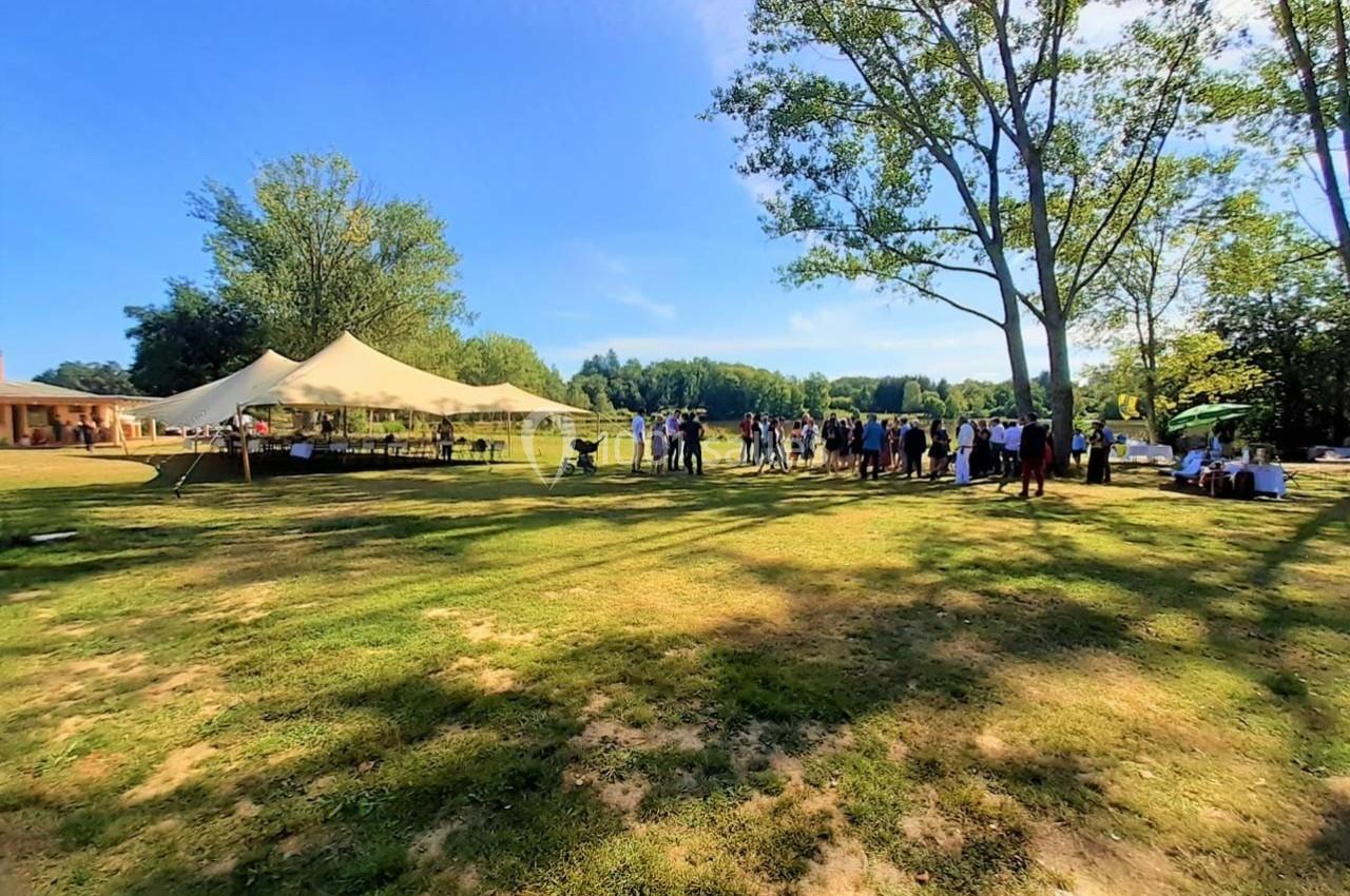 Groupe de personnes rassemblées dans un parc ensoleillé avec des tentes blanches et des arbres en arrière-plan.