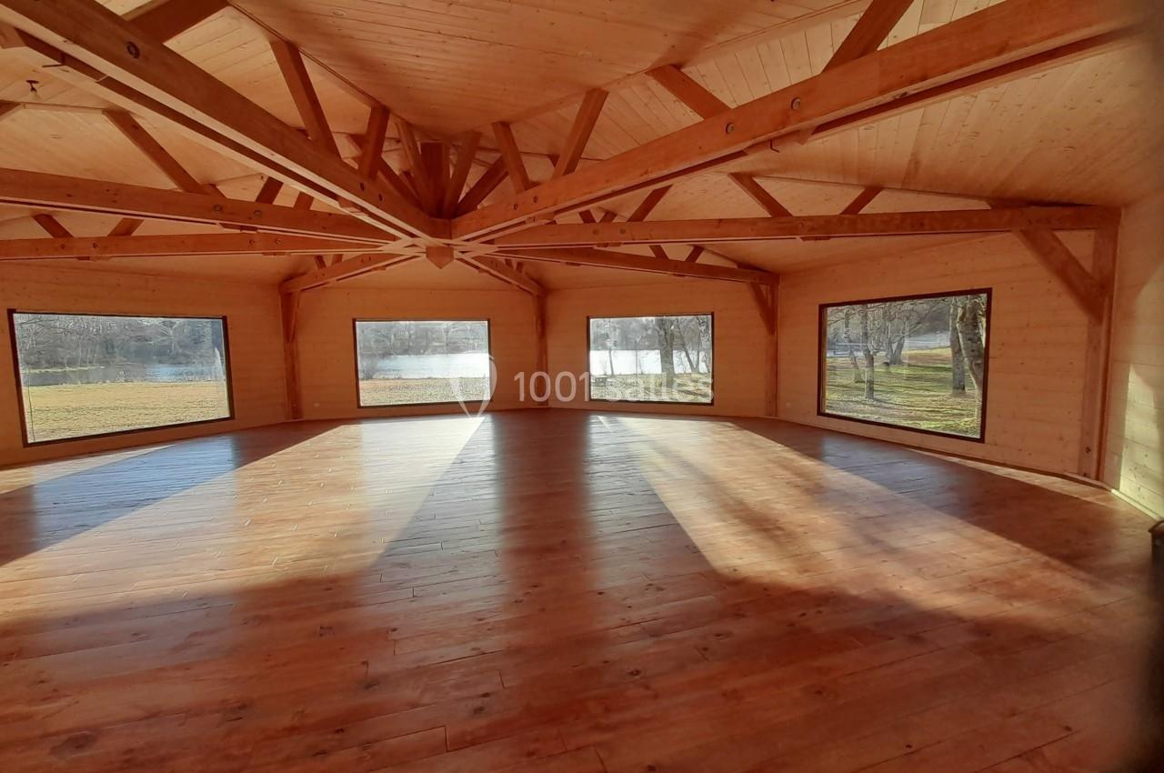 Salle en bois lumineuse avec de grandes fenêtres offrant une vue sur un paysage extérieur avec arbres et plan d'eau.