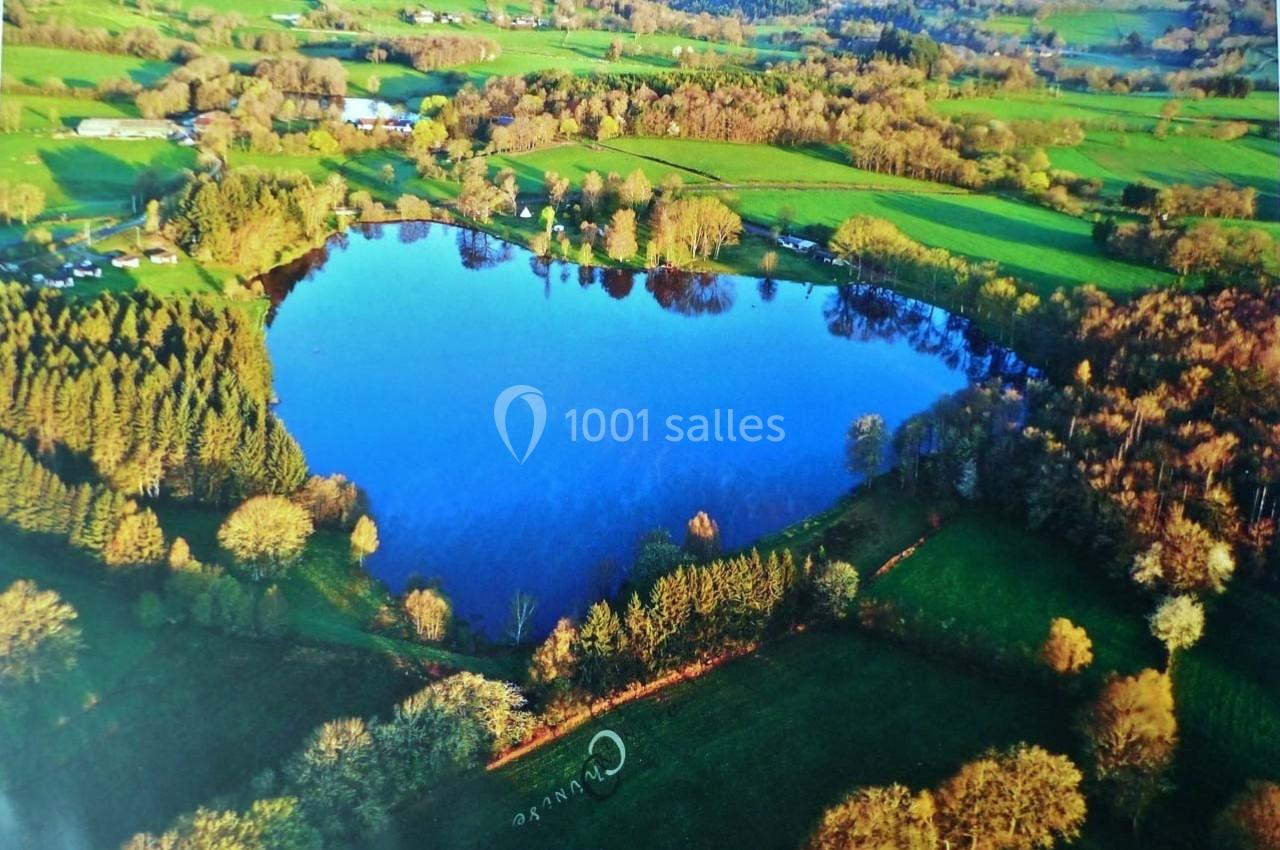 Vue aérienne d'un lac entouré de prairies verdoyantes, de forêts et de quelques habitations rurales.