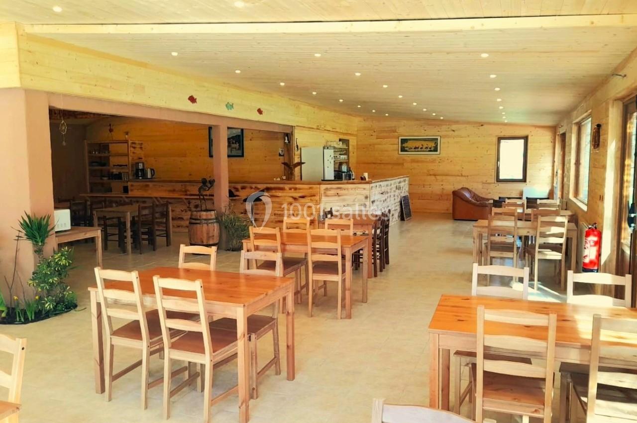 Salle lumineuse en bois clair avec tables et chaises en bois, un comptoir au fond et quelques plantes décoratives.