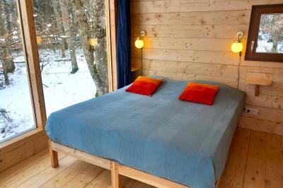 Cabane en bois avec toit en tuiles grises, grandes fenêtres et porte vitrée, située dans un espace arboré.