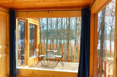 Cabane en bois avec toit en tuiles grises, grandes fenêtres et porte vitrée, située dans un espace arboré.