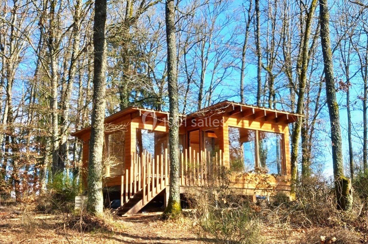 Cabane en bois entourée d'arbres dans une forêt, éclairée par une lumière naturelle.