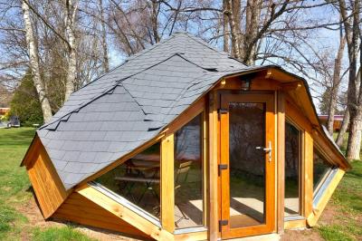 Cabane en bois avec toit en tuiles grises, grandes fenêtres et porte vitrée, située dans un espace arboré.