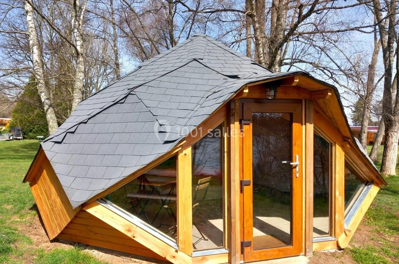 Cabane en bois avec toit en tuiles grises, grandes fenêtres et porte vitrée, située dans un espace arboré.