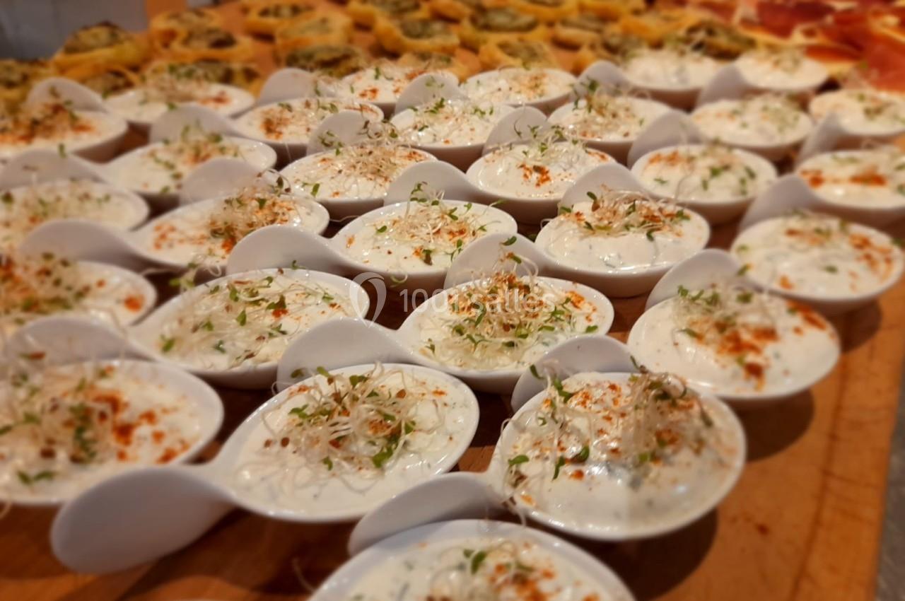 Petites cuillères en porcelaine garnies de crème blanche, herbes fraîches et paprika, disposées sur une table en bois.
