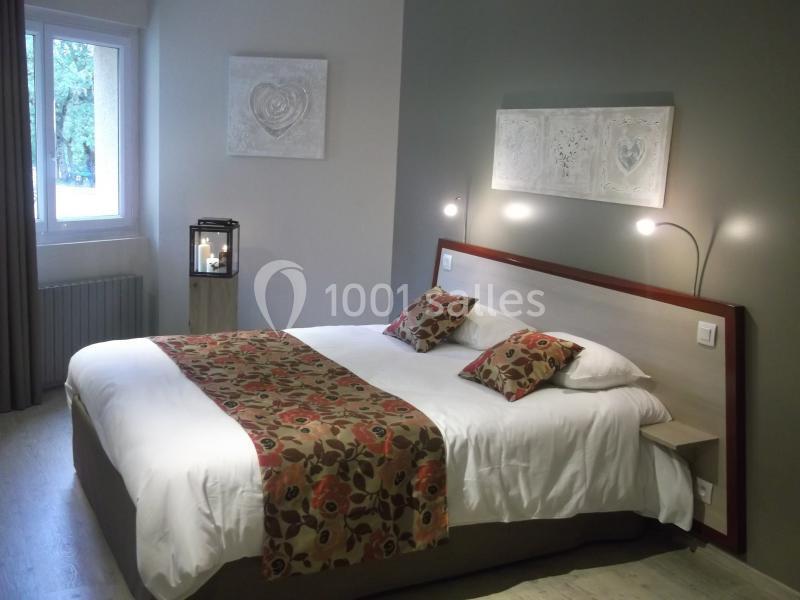 Chambre avec lit double, tête de lit en bois, décoration murale et lampe, fenêtre donnant sur un extérieur verdoyant.