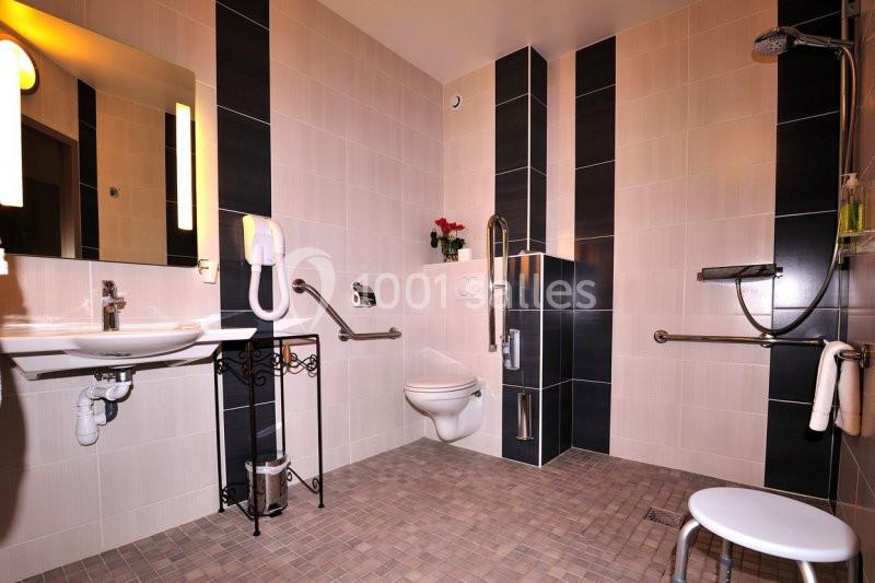 Salle de bain accessible avec douche à l'italienne, barres d'appui, lavabo adapté et toilettes surélevées.