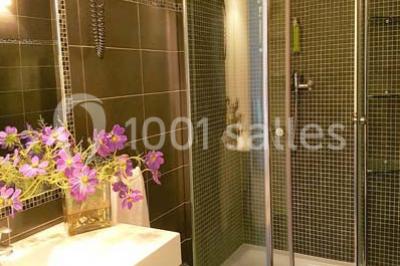 Salle de bain moderne avec douche arrondie, lavabo avec miroir éclairé et carrelage sombre.
