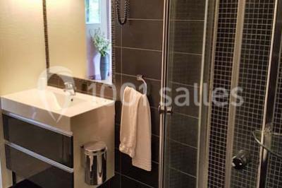 Salle de bain moderne avec douche arrondie, lavabo avec miroir éclairé et carrelage sombre.