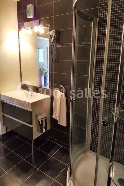 Salle de bain moderne avec douche arrondie, lavabo avec miroir éclairé et carrelage sombre.