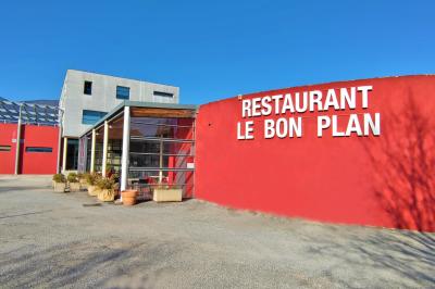 Façade d'un restaurant moderne avec terrasse, grandes baies vitrées et enseigne ’Restaurant Le Bon Plan’.