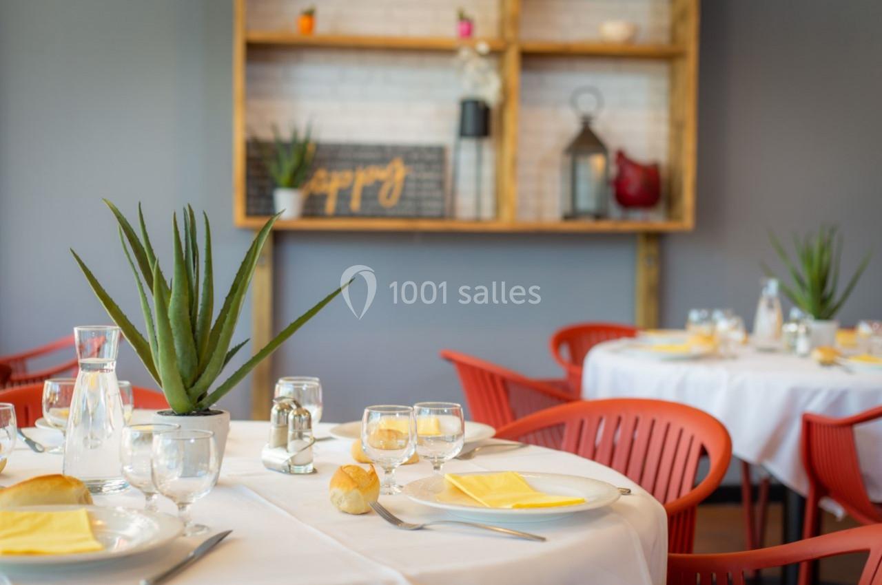 Salle de restaurant lumineuse avec tables dressées, chaises rouges et étagères décoratives en arrière-plan.