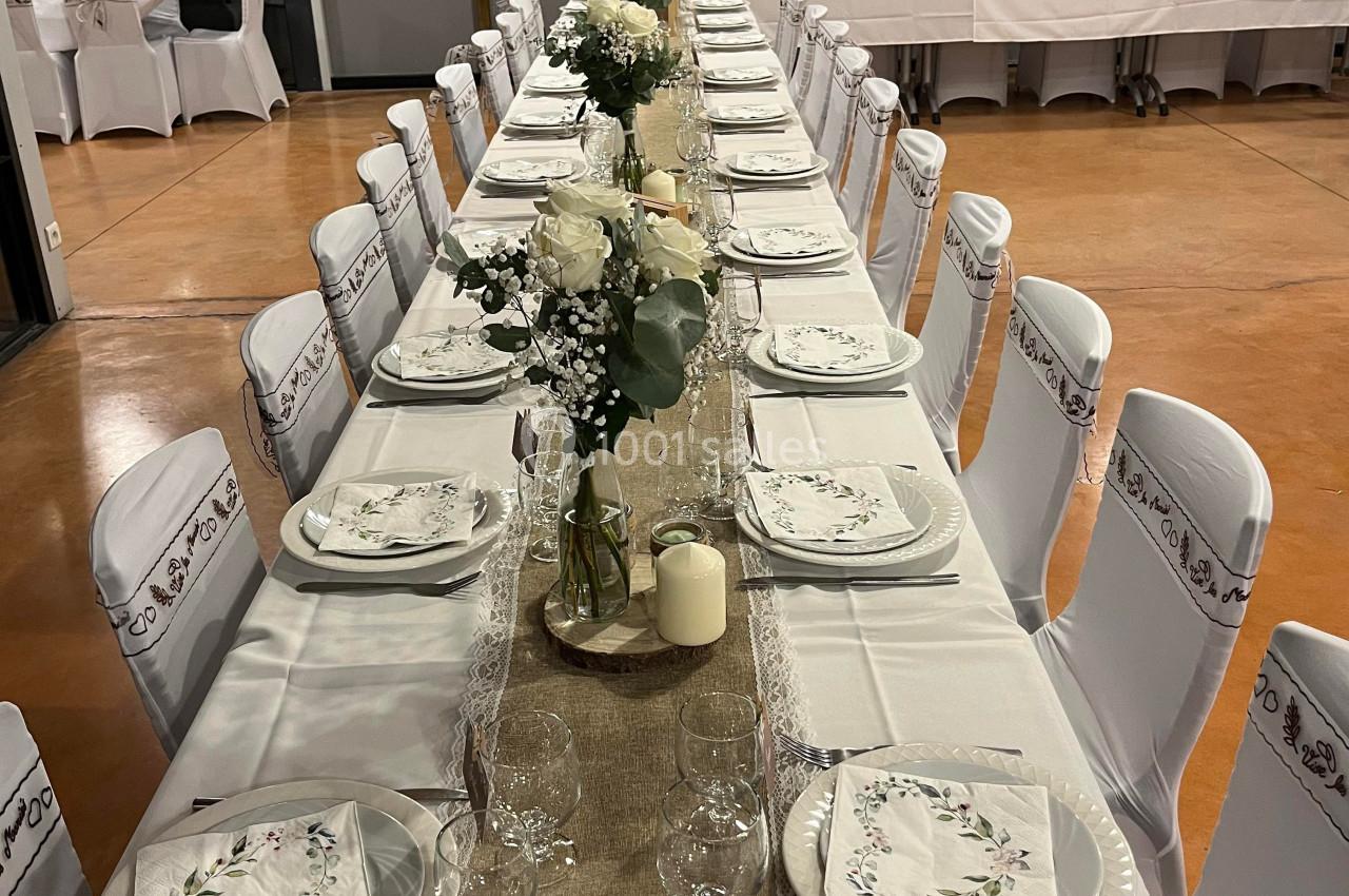 Table de réception décorée avec nappes blanches, chemins de table en lin, fleurs blanches et vaisselle élégante.