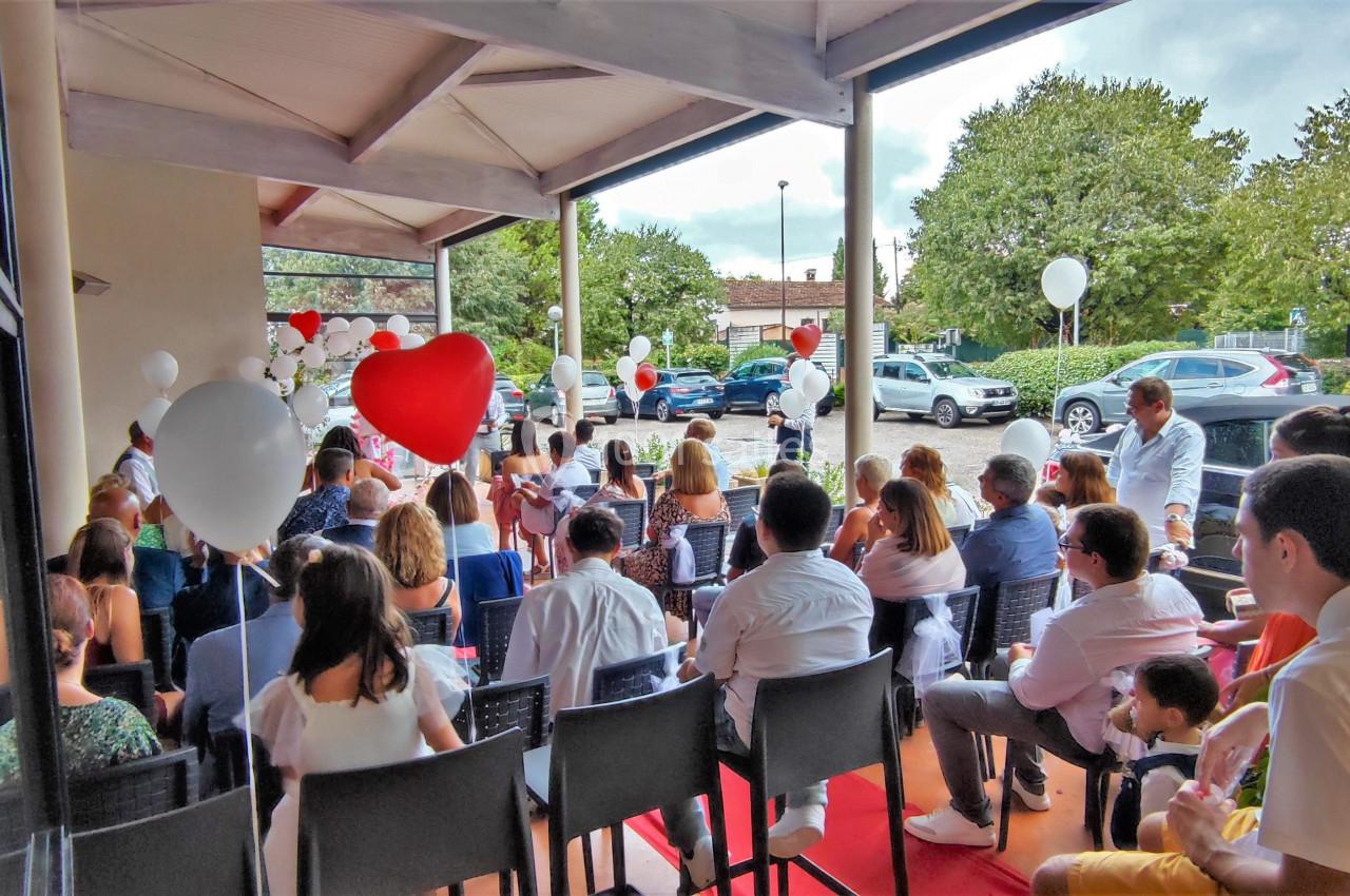 Groupe de personnes assises sous une terrasse couverte, entourées de ballons blancs et rouges, lors d'un événement en…