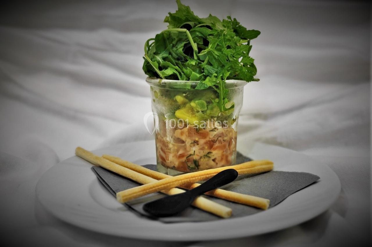 Verrine de tartare de saumon surmontée de roquette, accompagnée de gressins et d'une cuillère noire.