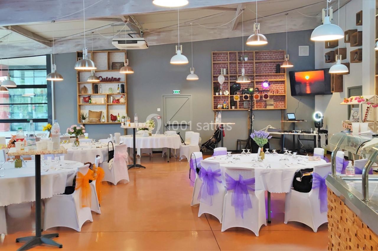 Salle de réception décorée avec des tables rondes, nappes blanches et chaises ornées de nœuds colorés.