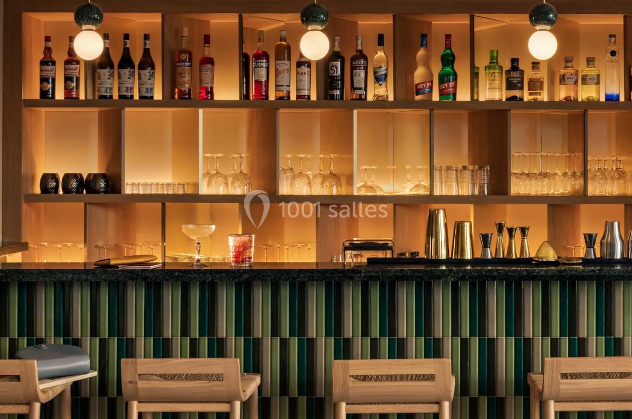 Bar avec comptoir en bois, étagères éclairées contenant bouteilles, verres et accessoires de mixologie.