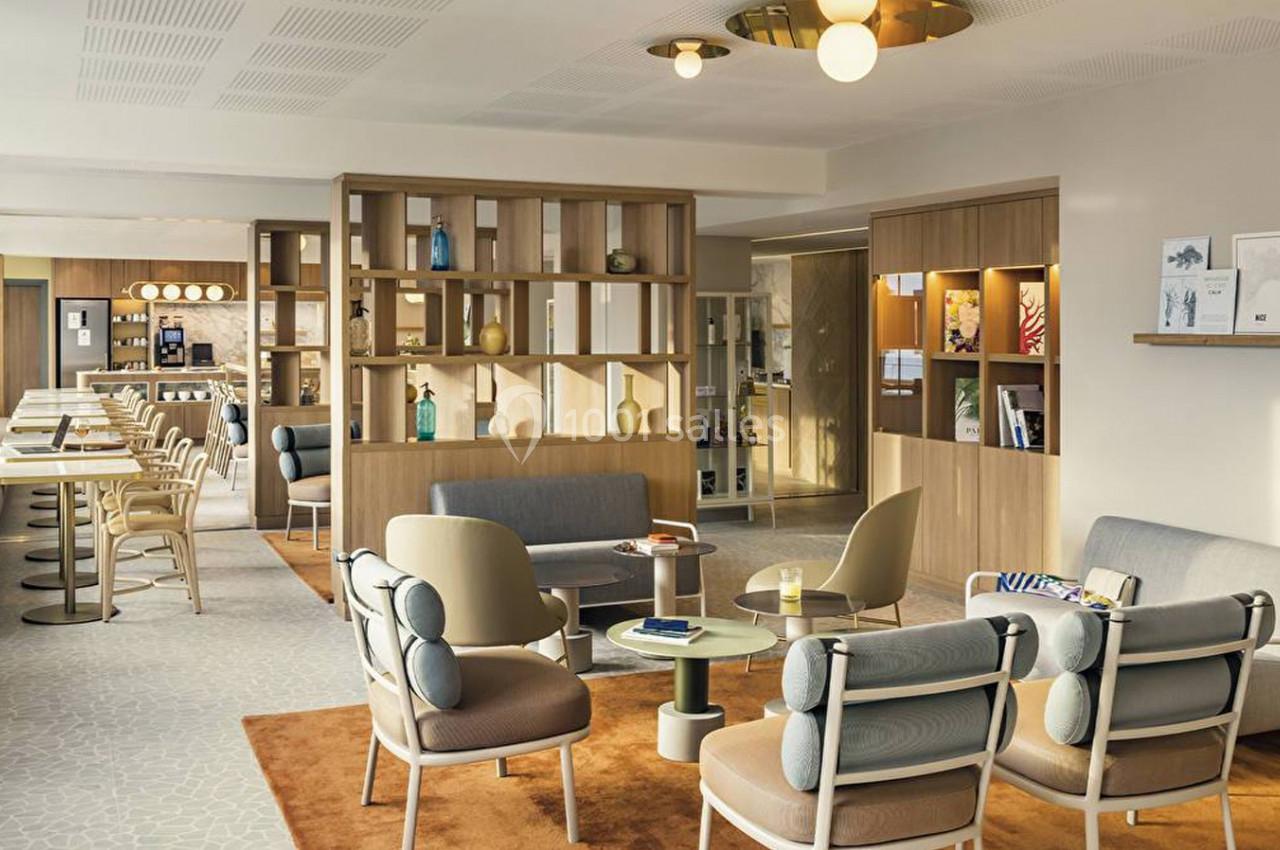 Espace intérieur lumineux avec mobilier moderne, fauteuils, tables et étagères en bois dans une ambiance conviviale.