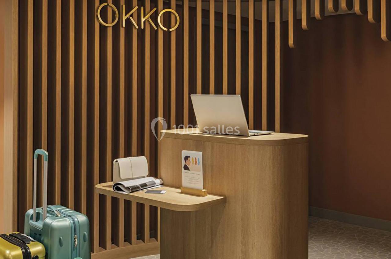 Comptoir d'accueil en bois avec un ordinateur portable, des bagages colorés posés à côté, dans un espace moderne.