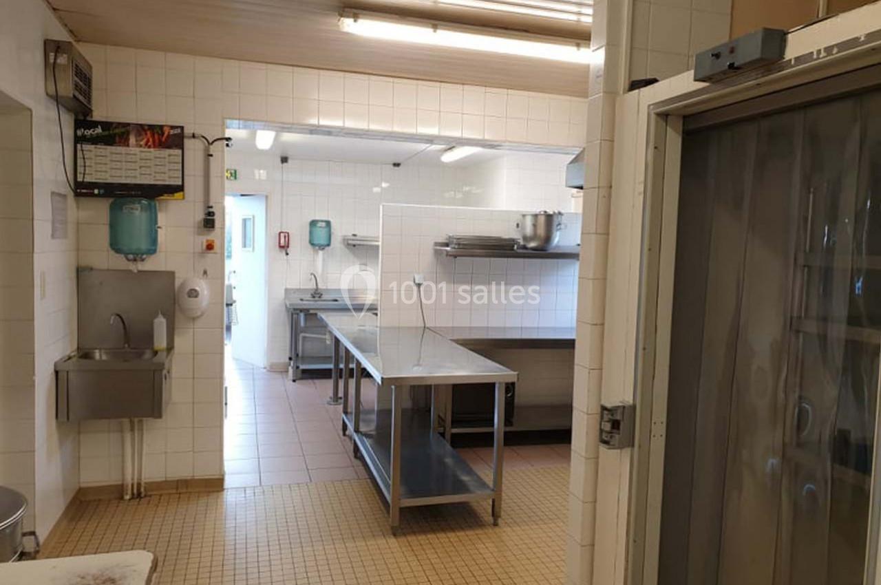 Cuisine professionnelle avec plans de travail en inox, murs carrelés blancs et équipements de nettoyage visibles.