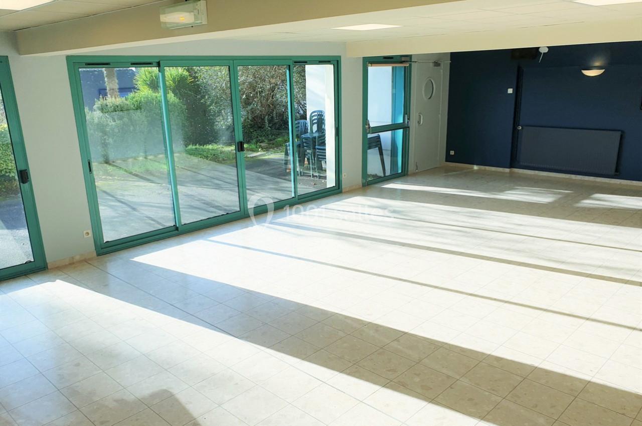 Salle lumineuse avec de grandes baies vitrées donnant sur un espace extérieur, sol en carrelage clair.