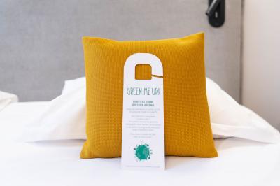 Un coussin jaune sur un lit blanc avec une pancarte suspendue indiquant un message écologique.