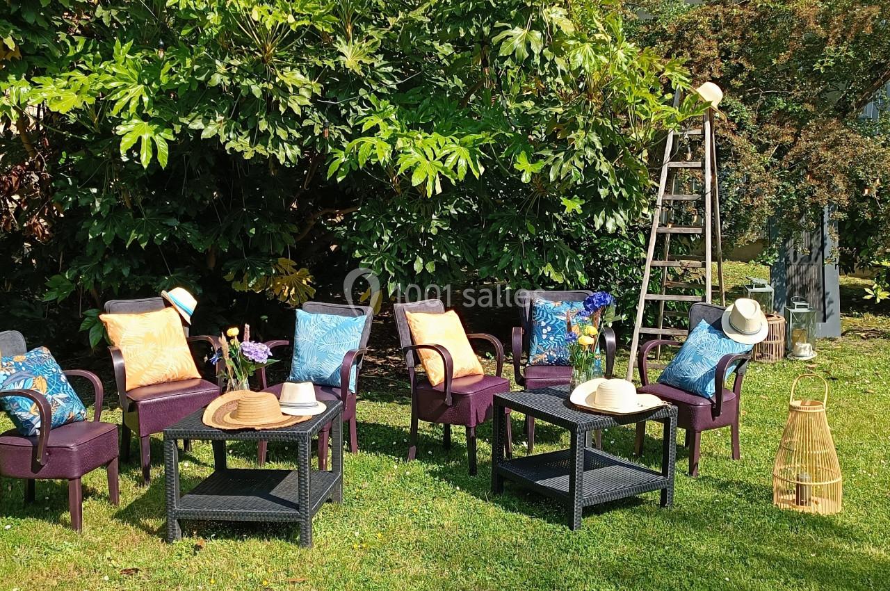 Chaises et tables noires avec coussins colorés disposées sur une pelouse, entourées d'arbres et d'éléments décoratifs.